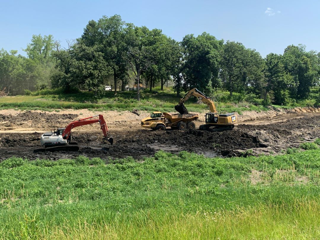 Large construction machines dredge sediment from inside of drained McFarland Lake