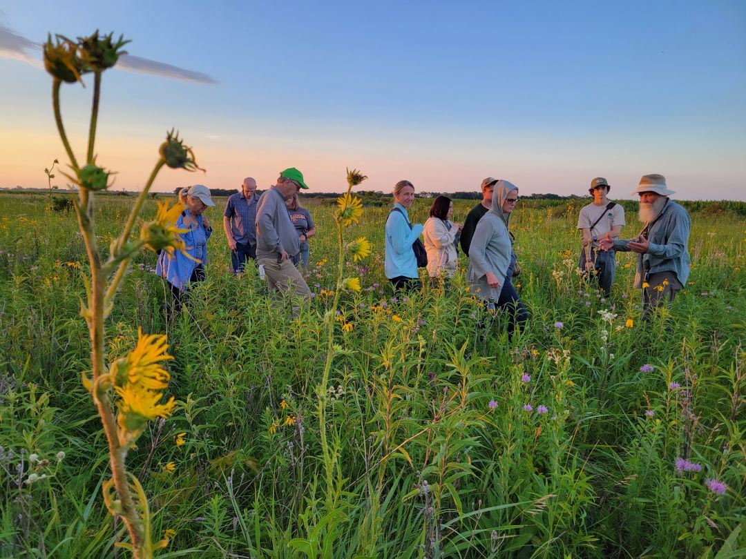 People stand in prairie at sunset as Dr. Rosburg leads public program