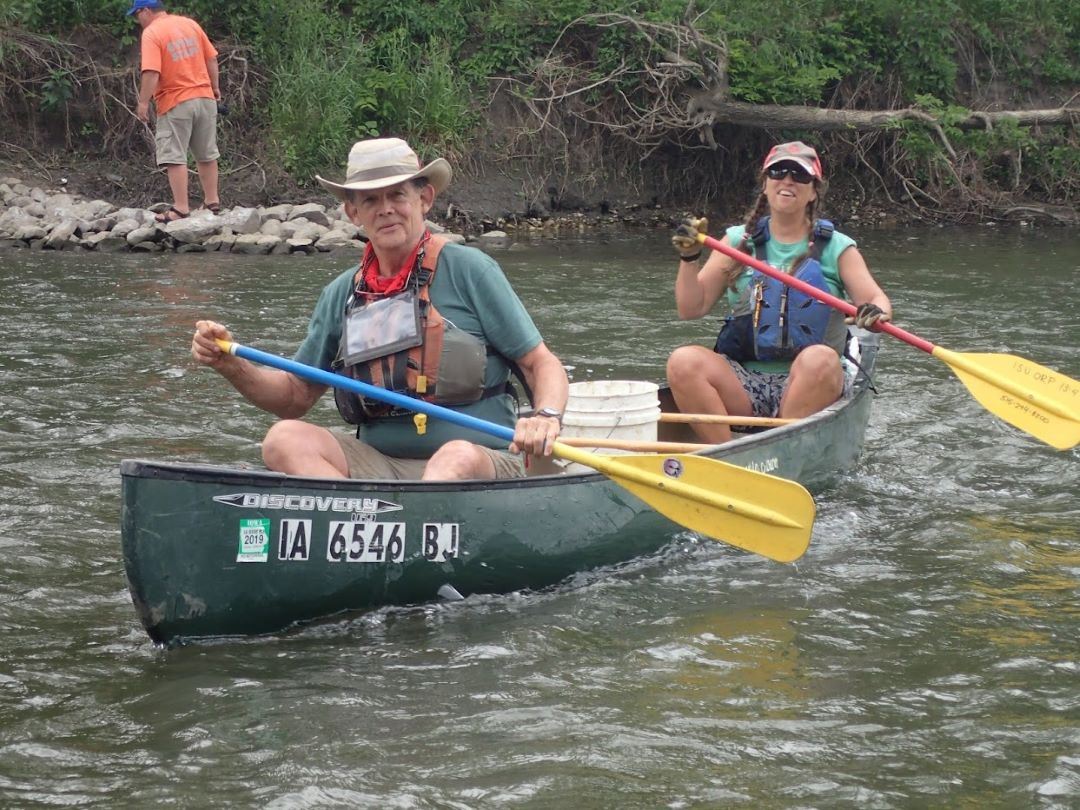 Volunteers paddle canoe in river while picking up trash