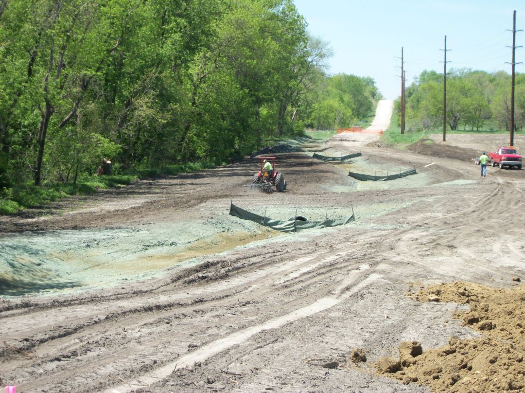 A tractor prepares a large, barren bare dirt roadside for planting