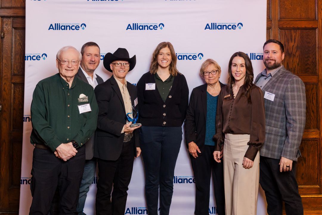 Group photo of adults wearing business clothing stand in front of photo backdrop holding award