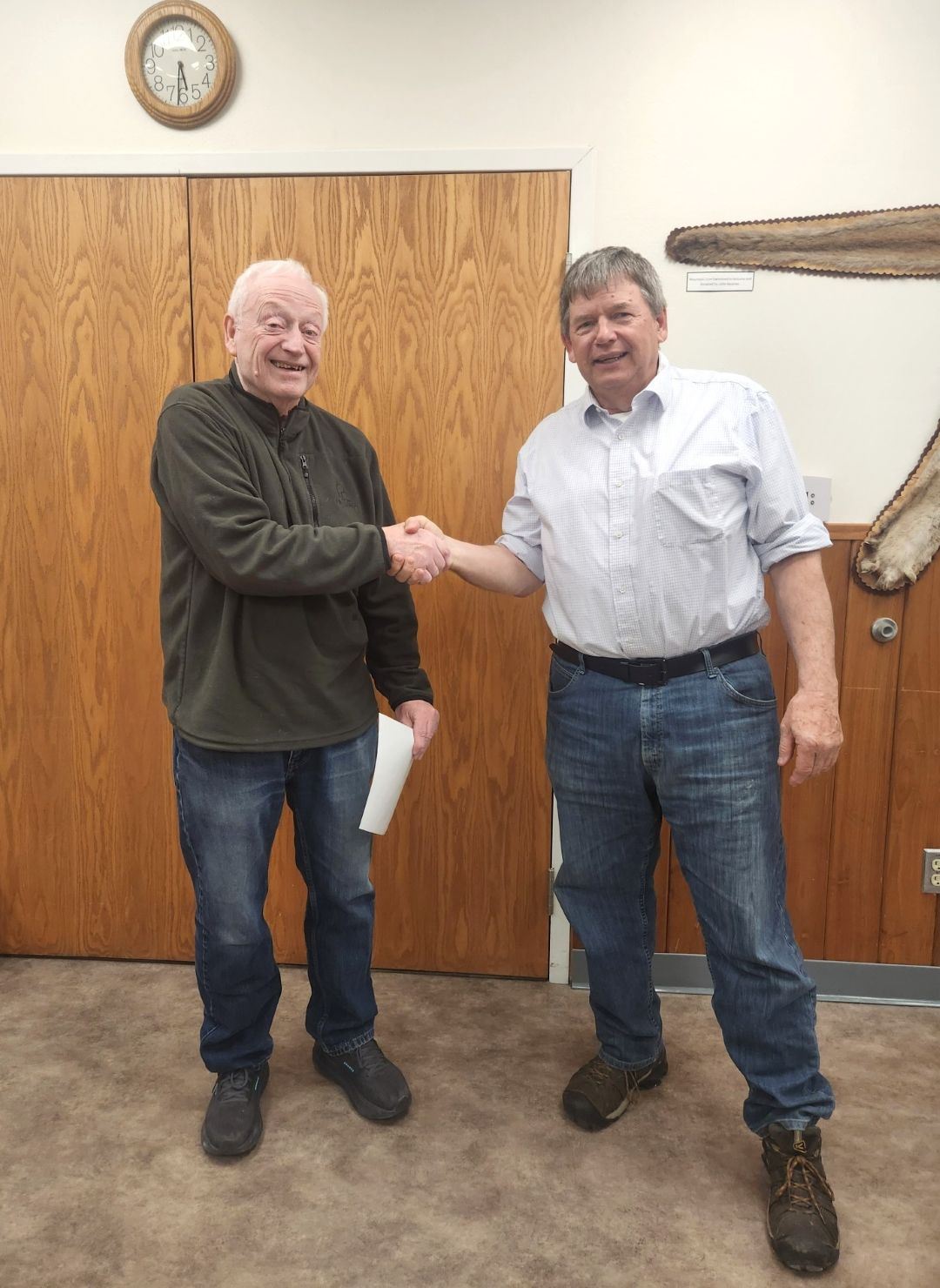 Older white male with white hair shakes hand of older white male with gray hair